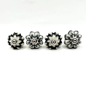 Peut inclure: Quatre boutons de meuble décoratifs avec un motif floral. Chaque bouton a une base blanche avec des détails noirs et un centre argenté. Les boutons sont disposés en rangée sur un fond blanc.