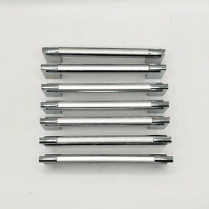 May include: Seven polished chrome cabinet pulls with a rectangular design. Each pull has a central, white-colored section and is arranged horizontally against a white background. These pulls are suitable for drawers or cabinets.