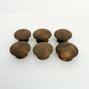 May include: A set of six round wooden knobs with a dark brown finish and visible wood grain. Each knob features a smooth, domed top surface and a cylindrical base, arranged in two rows of three on a plain, light-colored surface.
