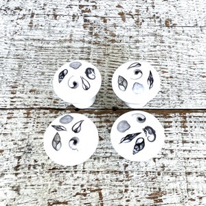 Peut inclure: Quatre sous-verres ronds en c&eacute;ramique blanche avec des illustrations en noir et blanc de coquillages, d'hippocampes et d'algues.