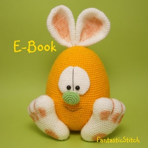 Könnte beinhalten: Ein gehäkeltes Osterhasen-Spielzeug in Form eines Eies. Der Hase ist gelb mit weißen Füßen und Ohren. Der Hase hat eine grüne Nase und schwarze Augen.