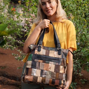 Puede incluir: Un bolso tote de cuero patchwork con una variedad de colores y texturas, incluyendo negro, marrón, verde y estampados de piel de serpiente. El bolso tiene asas negras y una cremallera en la parte superior. Un accesorio elegante y único.