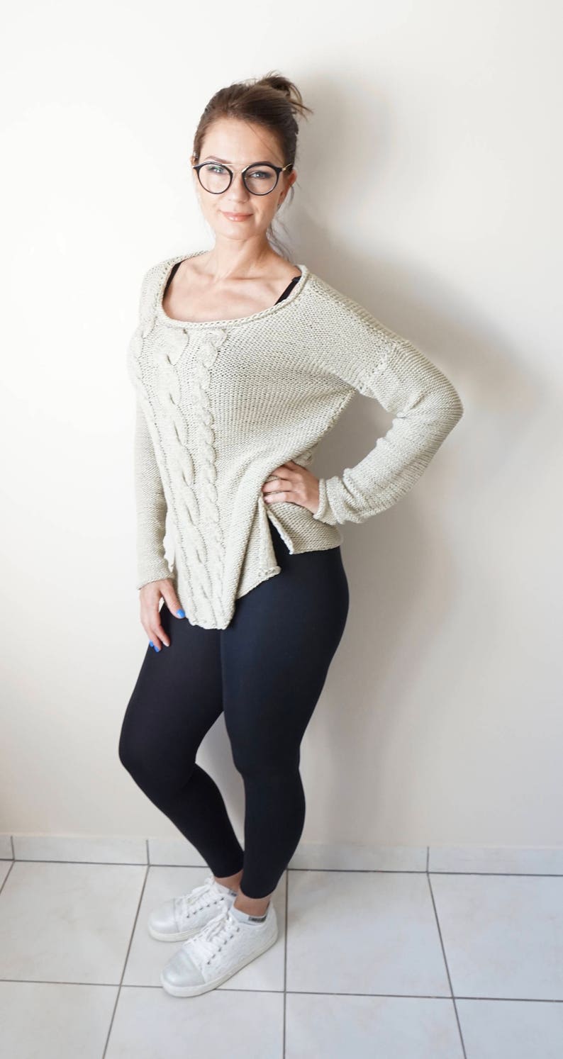 May include: A woman wearing a light beige cable knit sweater with black leggings and white sneakers.