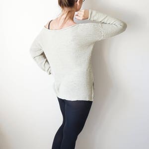 May include: A woman wearing a light beige knitted sweater, black leggings, and white sneakers. She is standing with her back to the camera.