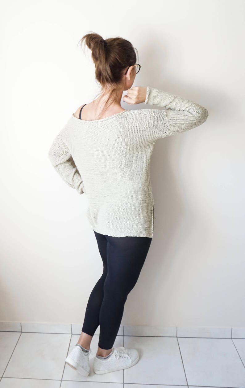 May include: A woman wearing a light beige knitted sweater, black leggings, and white sneakers. She is standing with her back to the camera.