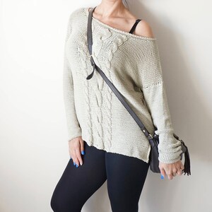 May include: A woman wearing a light beige cable knit sweater with a black crossbody bag, black leggings, and white sneakers.