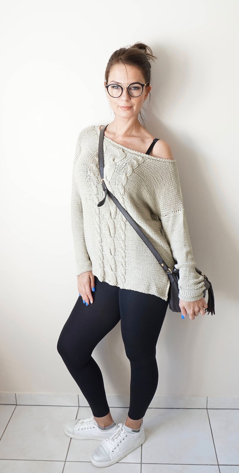 May include: A woman wearing a light beige cable knit sweater with a black crossbody bag, black leggings, and white sneakers.