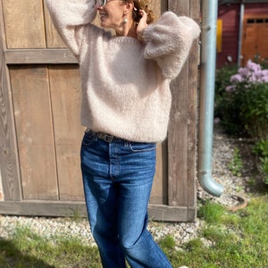Puede incluir: Una mujer con un su&eacute;ter rosa claro peludo con un cintur&oacute;n marr&oacute;n y jeans azules. Lleva zapatillas blancas y gafas de sol.