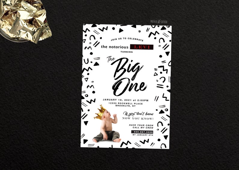 May include: A white and black geometric patterned invitation for a first birthday party. The invitation says "Join us to celebrate the notorious Levi turning The Big One" and includes the date and time of the party. The invitation also features a photo of a baby wearing a gold crown.