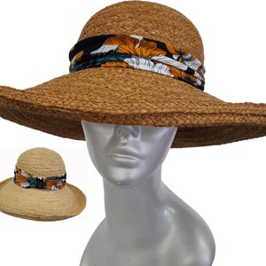 Puede incluir: Sombrero de paja marrón con ala ancha y banda decorativa. La banda presenta un estampado floral en naranja, blanco y verde sobre fondo azul marino. El sombrero tiene una copa redonda y un ala ancha, ideal para la protección solar.