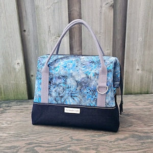May include: A blue and gray floral patterned tote bag with black fabric trim and a gray fabric handle. The bag has a label that reads "My Needle Crafts".