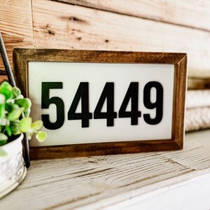 May include: A wooden framed sign with a white background and black numbers that read "54449".