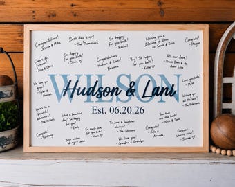 Pode incluir: Uma placa retangular para livro de visitas com moldura de madeira e fundo branco, apresentando o texto grande em azul claro WILSON, o texto em letra cursiva azul escuro Hudson & Lani e a data Est. 06.20.26, rodeados por mensagens de felicitações.