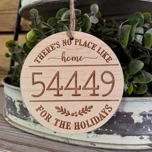 May include: A round wooden ornament with the text "There's no place like home 5449 for the holidays" in brown lettering. The ornament is hanging from a string.