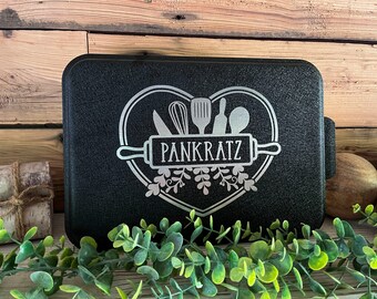 May include: Black baking pan with a silver heart design featuring kitchen utensils and the text "Pankratz" on a rolling pin.