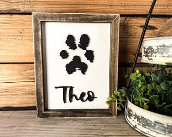 May include: A framed wooden sign with a black paw print and the name "Theo" written in black lettering.