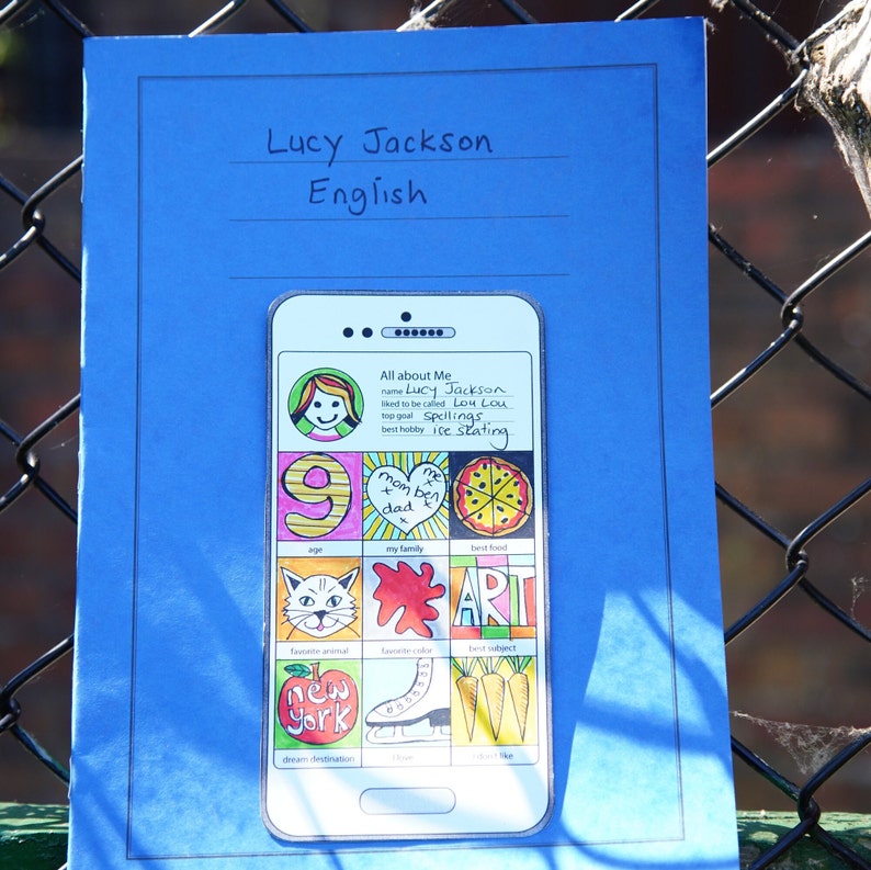 May include: A blue sheet of paper with the words "Lucy Jackson" and "English" written at the top. A drawing of a smartphone screen with the words "All about Me" and information about Lucy, including her name, nickname, goals, hobbies, and favorite things.
