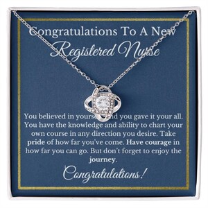 May include: A silver-colored necklace with a pendant in the shape of a four-leaf clover, encrusted with clear crystals. The necklace is presented in a gift box with text that reads "Congratulations To A New Registered Nurse."