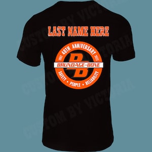 May include: Black t-shirt with an orange circle graphic. The graphic says "40th Anniversary 1983-2023" and "Brundage-Bone". Inside the circle is a large black "B". Below the circle are the words "Safety, People, Reliability". The text "LAST NAME HERE" is at the top of the shirt.
