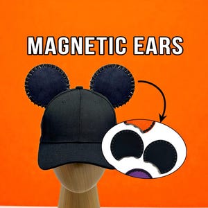 May include: Black baseball cap with attached magnetic ears. The ears are dark blue with silver accents. The image includes the text "MAGNETIC EARS" in white block letters against an orange background. An inset shows the magnetic ear design.