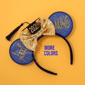 May include: Blue and gold glitter mouse ears with a black graduation cap that says "2023" and a gold bow. The ears have the text "Class of 2023" on one ear and "Happy" on the other.