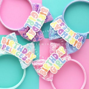 Puede incluir: Tres lazos para diadema coloridos con el texto "Birthday Girl", "Birthday Princess" y "Birthday Princess" en letras arco&iacute;ris. Las diademas est&aacute;n hechas de tela de lentejuelas blancas y azules.