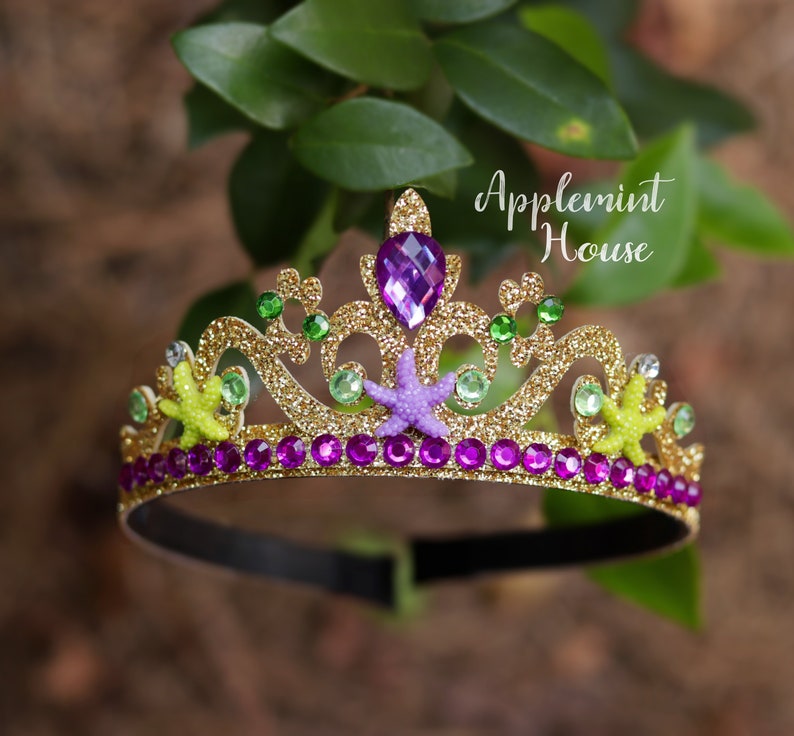 May include: Gold glitter headband with a purple gem, green and yellow starfish, and purple rhinestones. The headband says "Applemint House".