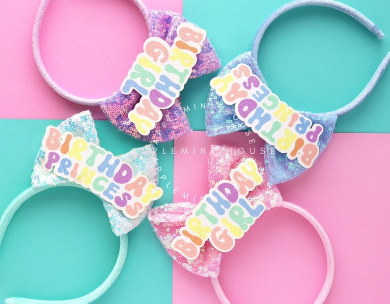 Puede incluir: Tres lazos para diadema coloridos con el texto "Birthday Girl", "Birthday Princess" y "Birthday Princess" en letras arco&iacute;ris. Las diademas est&aacute;n hechas de tela de lentejuelas blancas y azules.