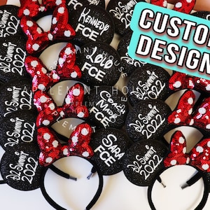 May include: A selection of black glitter mouse ear headbands with red sequined bows. Each ear features white text with names and "D2 Summit 2022". A sign reads "CUSTOM DESIGN".