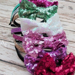 Pu&ograve; includere: Un set di cinque cerchietti per capelli scintillanti con fiocchi. I cerchietti sono in tonalit&agrave; di verde, bianco, viola e rosa. I fiocchi sono fatti di paillettes.