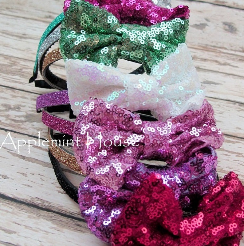 Pu&ograve; includere: Un set di cinque cerchietti per capelli scintillanti con fiocchi. I cerchietti sono in tonalit&agrave; di verde, bianco, viola e rosa. I fiocchi sono fatti di paillettes.