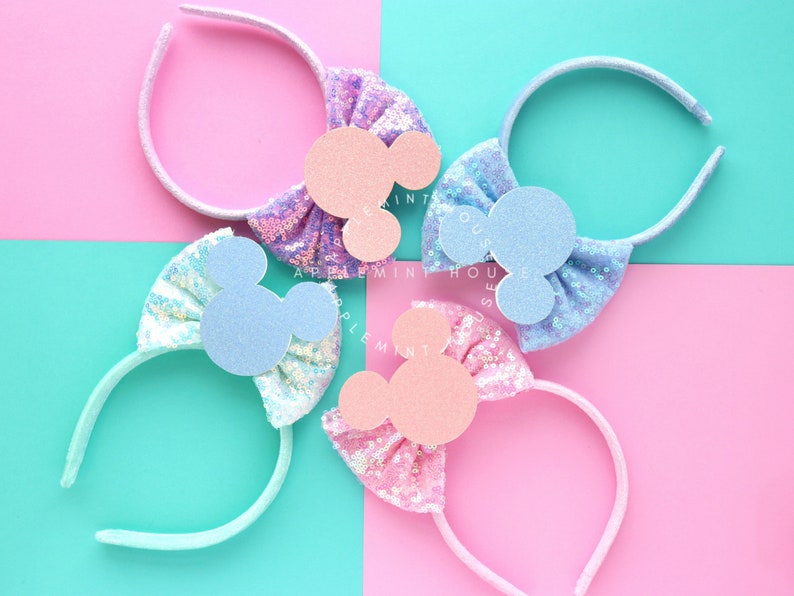 Puede incluir: Tres diademas de colores pastel con lazos de lentejuelas y orejas de Mickey Mouse de fieltro. Las diademas son azul claro, rosa y morado.
