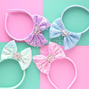 Puede incluir: Cuatro diademas con lazos brillantes y un dije de corona. Los lazos son en tonos de azul, rosa y morado.