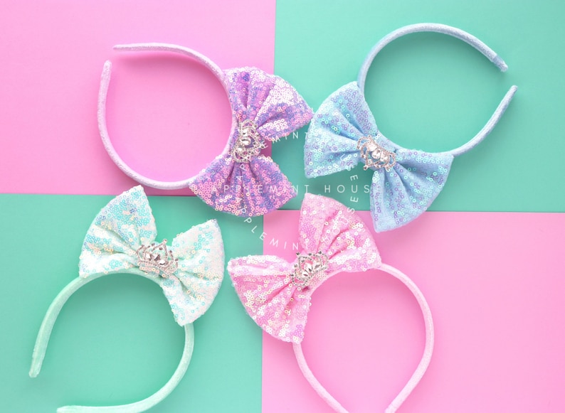 Puede incluir: Cuatro diademas con lazos brillantes y un dije de corona. Los lazos son en tonos de azul, rosa y morado.