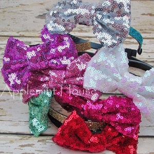 Pu&ograve; includere: Un set di cinque fiocchi per capelli con paillettes in vari colori, tra cui argento, rosa, bianco, verde acqua e rosso. Ogni fiocco &egrave; attaccato a un cerchietto nero con un bordo dorato.