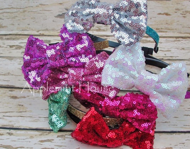 Pu&ograve; includere: Un set di cinque fiocchi per capelli con paillettes in vari colori, tra cui argento, rosa, bianco, verde acqua e rosso. Ogni fiocco &egrave; attaccato a un cerchietto nero con un bordo dorato.