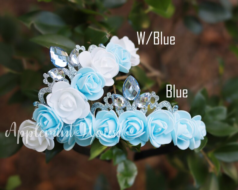 May include: Two flower crowns with blue and white fabric flowers and silver glitter trim. One crown has all blue flowers and the other has white and blue flowers. The text "W/Blue" and "Blue" are visible in the image.