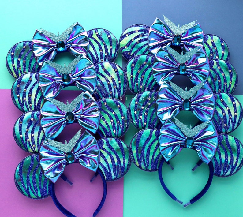 Op de afbeelding: Set van 10 blauwe en groene, iriserende Minnie Mouse oren met een zebraprint. De oren zijn versierd met een grote strik en glitter.