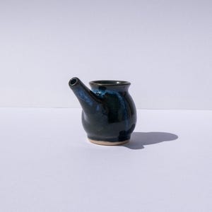 May include: A dark blue and green ceramic neti pot with a spout. The pot is glazed and has a smooth finish.