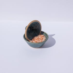 May include: A blue and brown ceramic salt cellar with a lid, filled with pink Himalayan salt.