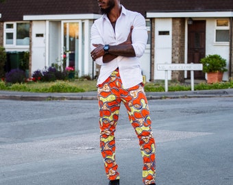 Puede incluir: Una persona con una camisa blanca y pantalones naranjas estampados con diseños amarillos y azules. La persona también lleva gafas de sol negras y zapatos negros. La imagen está tomada al aire libre.
