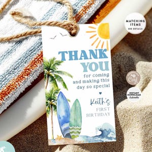 May include: A beach-themed gift tag with the words "THANK YOU" in blue, featuring palm trees, surfboards, and a sun illustration. The tag is for a first birthday and includes the name "Keith". The tag is tied with a natural twine.