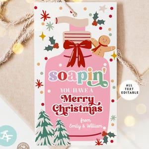 May include: A pink Christmas gift tag featuring a soap dispenser design with the text "soapin'" and "Merry Christmas". The tag includes a gingerbread man, Christmas trees, and holly accents. The text is editable.