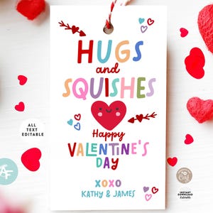 May include: A white Valentine's Day gift tag with the words "HUGS and SQUISHES" in colorful letters. The tag features a smiling heart, arrows, and the text "Happy VALENTINE'S DAY". The tag is decorated with small red hearts and a red and white string.