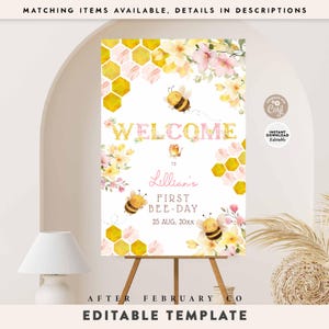 May include: A welcome sign for a first birthday party, featuring a bee theme. The sign includes the text "WELCOME" and "Lillian's FIRST BEE-DAY" with decorative bees, flowers, and honeycomb patterns. The sign is displayed on a wooden easel.