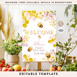 May include: A welcome sign with a bee theme, featuring the text "WELCOME" in pink and gold, with illustrations of bees and honeycomb patterns. The sign is on an easel, surrounded by flowers and greenery. The text "Lillian's FIRST BEE-DAY" is also visible.