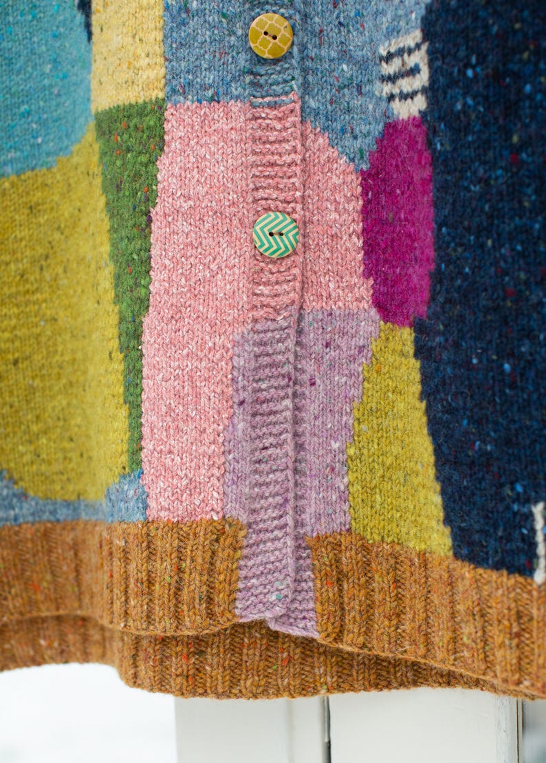 Może przedstawiać: Zbliżenie kolorowego kardiganu w stylu patchwork. Sweter ma r&oacute;żne kolory, w tym r&oacute;żowy, niebieski, zielony, ż&oacute;łty i fioletowy. Ma dwa ozdobne guziki i prążkowany brązowy d&oacute;ł.