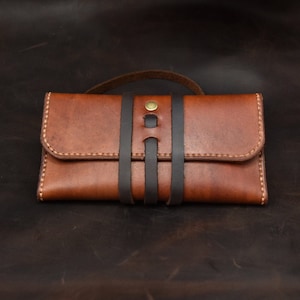 Peut inclure: Un portefeuille en cuir marron avec des lanières en cuir noir et une fermeture à bouton en laiton.