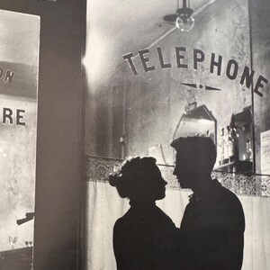 May include: A black and white photograph of a couple silhouetted against a window with the word "TELEPHONE" written on the glass.