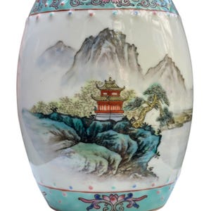 May include: A white ceramic vase with a blue and green floral design around the top and bottom. The vase features a painted scene of a mountain range with a red pagoda and a pine tree.